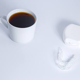 an Invisalign aligner next to a cup of coffee