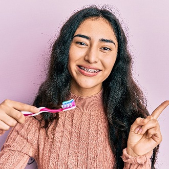 Girl with braces smiling while holding toothbrush