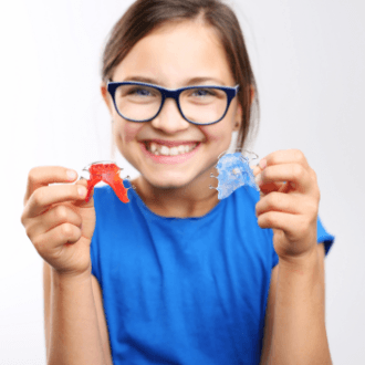 Smiling preteen girl holding up orthodontic appliances