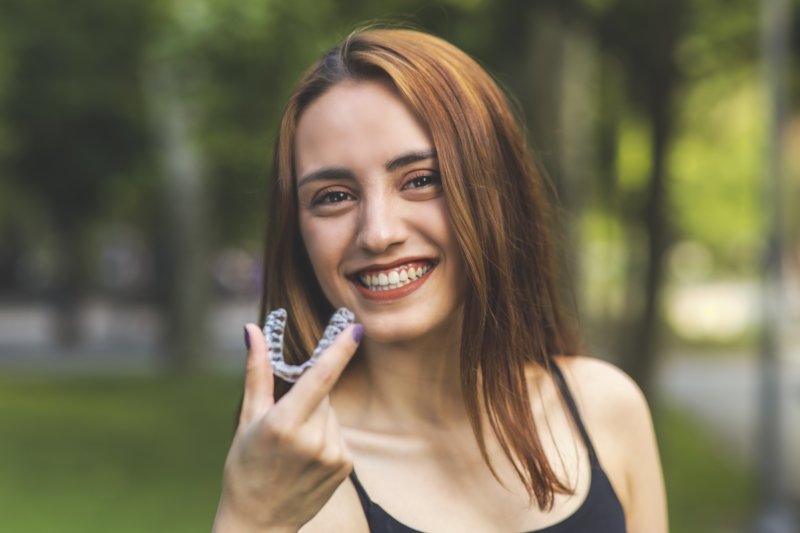 Closeup of woman smiling while holding Invisalign trays