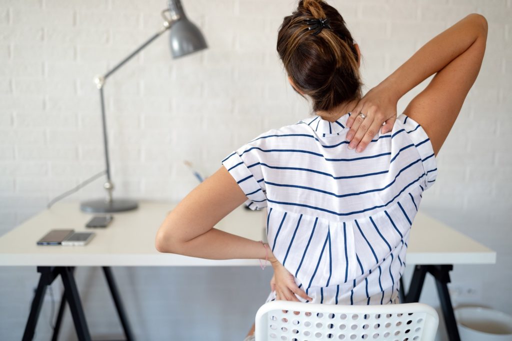 Woman experiencing back soreness after slouching at desk