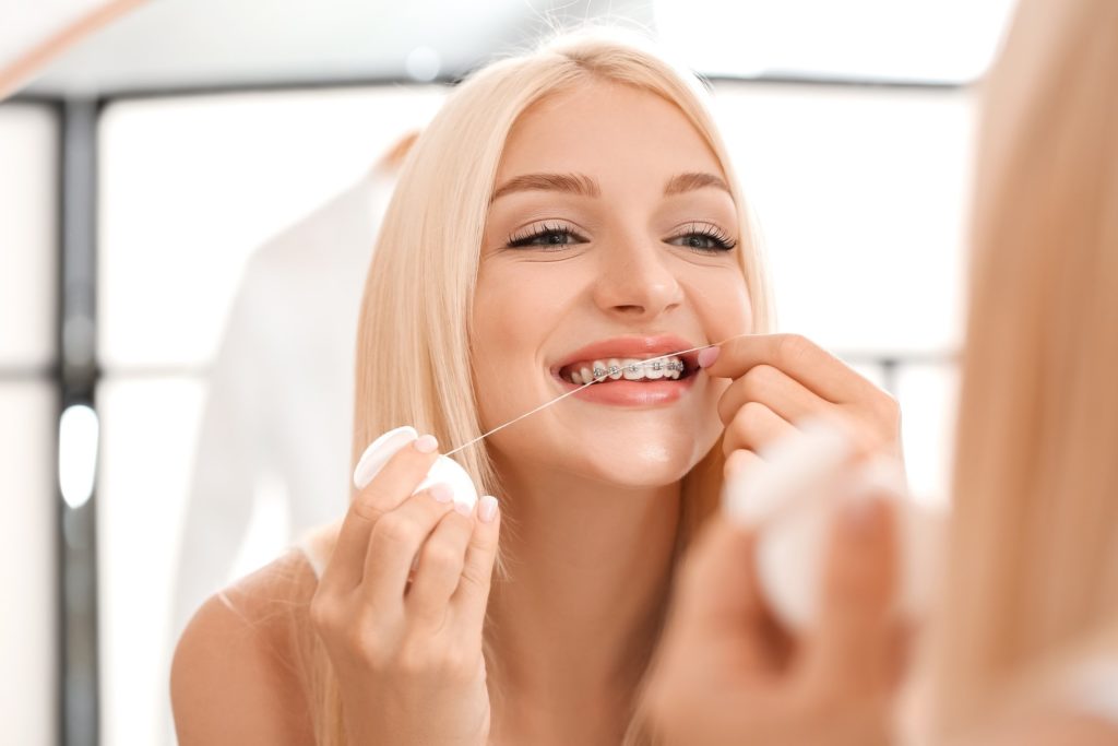 Closeup of woman with braces smiling while flossing