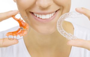 a patient smiling and holding their retainer 
