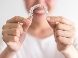 a patient smiling and holding their Invisalign aligner